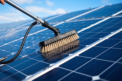 Szczotka z wodą czyszcząca powierzchnię paneli fotowoltaicznych w słoneczny dzień.