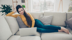 Kobieta odpoczywająca na jasnym narożniku w salonie, korzystająca z laptopa